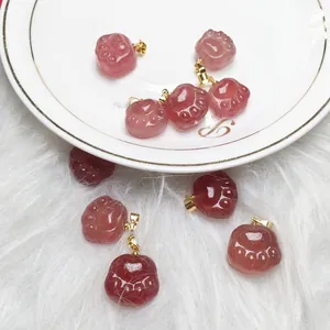 Macro detail of strawberry quartz cat paw charms with gold clips on a white ceramic plate
