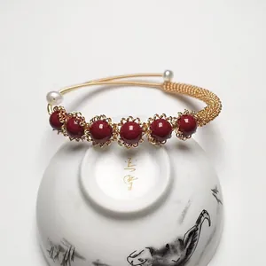 Detail of handmade gold-wrapped cinnabar bracelet with pearls on vintage porcelain