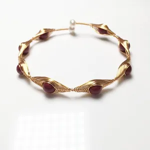 Detail of handmade wire-wrapped gold bracelet with red garnet beads and a white pearl accent