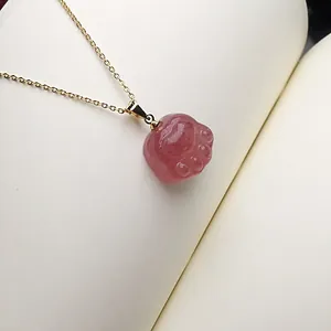 Macro shot of pink strawberry quartz cat paw pendant with golden chain on a notebook