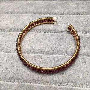 Macro detail of handmade gold wire wrapped garnet bangle with white pearl accents