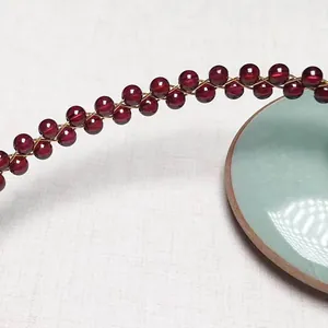 Detailed macro view of garnet beads woven with 14K gold filled wire on ceramic plate