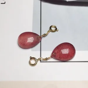 Dettaglio di orecchini a goccia in cristallo fragola rosso con filo dorato e cerchi a molla