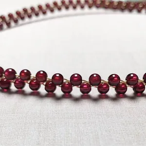Macro detail of wine red garnet beads woven with 14K gold-filled wire on white fabric
