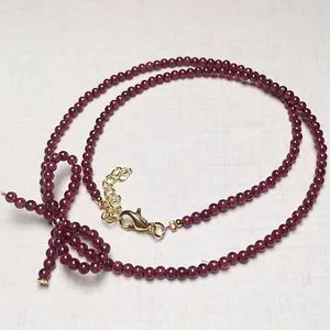 Detailed macro view of dark red garnet beaded necklace with gold lobster clasp and bow charm
