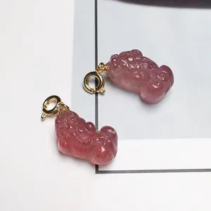 Dettaglio di ciondoli Pixiu in quarzo rosa con ganci in metallo dorato su carta bianca