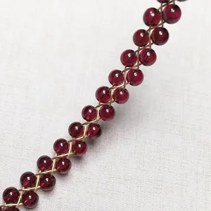 Detailed close-up of woven red garnet beads with gold-filled wire on a textured surface