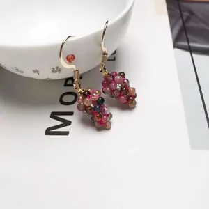 Macro shot of colorful beaded grape-shaped earrings hanging on a white ceramic bowl