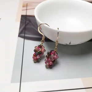 Detailed view of colorful tourmaline grape-shaped earrings hanging on a white porcelain cup