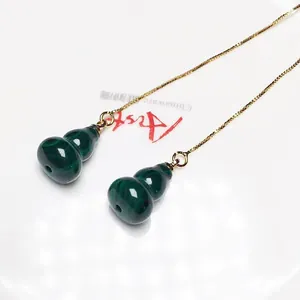 Detail of malachite gourd drop earrings with fine gold chain on white ceramic