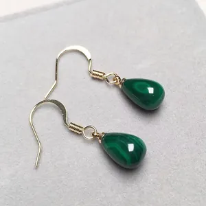 Dettaglio di orecchini a gancio dorati con pietre di malachite verde a goccia e venature