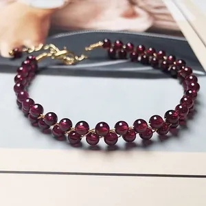 Detail of garnet red double-row beaded bracelet with gold lobster clasp on magazine backdrop