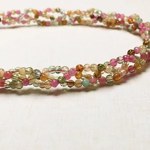 Détail macro d'un collier en perles de tourmaline multicolores au design tressé