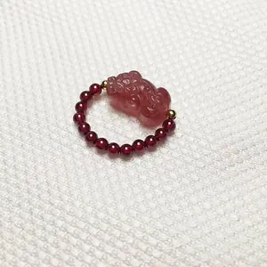 Detail of garnet beaded ring featuring a translucent carved strawberry crystal Pixiu charm