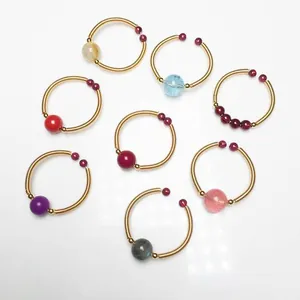 Flat lay detail of eight colorful gemstone beaded rings with gold spiral spring bands