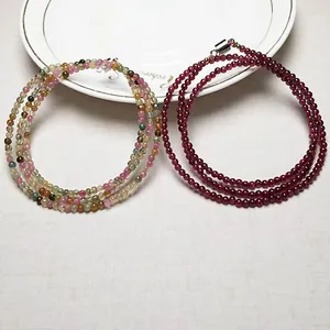 Close-up of tourmaline and garnet beads with silver clasps on a white ceramic plate