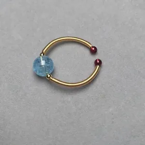 Macro detail of sky blue gemstone bead and golden wire wrap on an adjustable ring