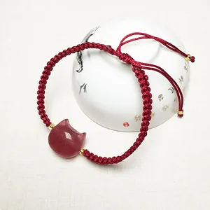 Macro shot of red braided rope bracelet with pink cat-head gemstone and golden beads