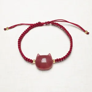 Detailed shot of handmade red cord bracelet with strawberry quartz cat charm and gold beads