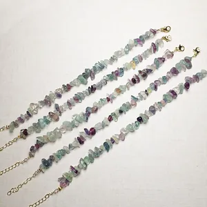 Detail of five multi-colored fluorite chip bracelets with golden lobster clasps on white fabric