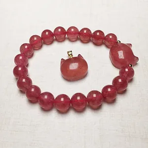 Macro detail of strawberry quartz beaded bracelet with carved fox charm and golden accents