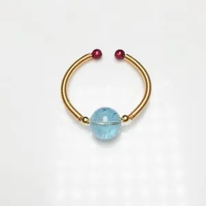 Detail of 14K gold wire wrapped ring with red beads and blue translucent gemstone