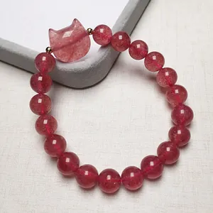 Macro view of strawberry quartz bracelet showing translucent beads and cat head charm