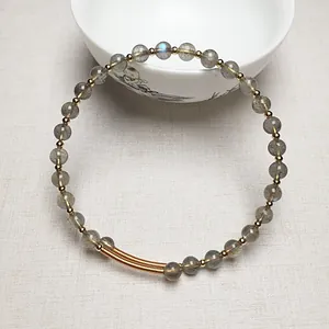 Détail d'un bracelet en perles de labradorite avec perles dorées sur fond de tissu neutre