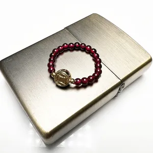 Close-up of garnet beaded ring with a 14K gold-plated coin charm on a textured surface