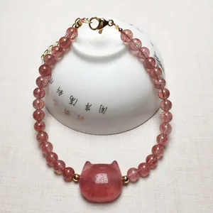 Detail of pink strawberry quartz bracelet with cat-shaped stone and gold lobster clasp