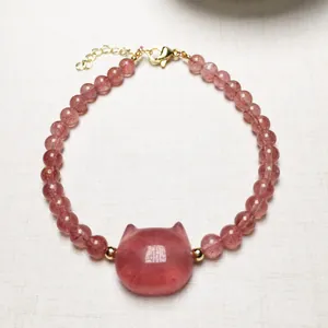 Macro shot of strawberry quartz beaded bracelet with a cat-shaped stone and gold lobster clasp