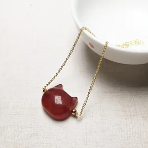 Close-up of a strawberry quartz cat pendant on a delicate gold chain over a soft cloth
