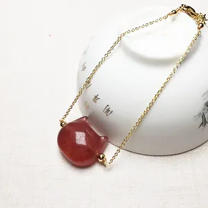 Detailed shot of a gold strawberry quartz bracelet featuring a carved cat head pendant