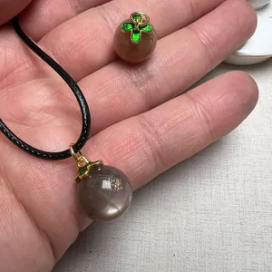 Detailed macro of a sunstone pendant with golden four-leaf clover enamel and leather cord