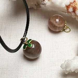 Macro shot of sunstone pendant with green enamel clover cap and black woven cord
