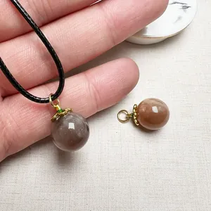 Polished sunstone crystal ball pendant necklace with golden petal cap on woven cord
