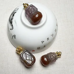 Hand-carved Auralite 23 PiXiu pendants with gold crown clasps on a white porcelain bowl