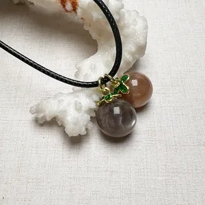 Close-up of sunstone pendant with grey moonstone bead and green enamel gold cap