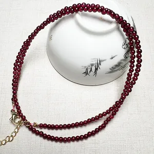 Macro detail of red garnet bead necklace featuring a gold lobster clasp and extension chain