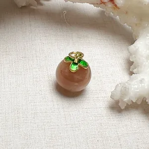 Macro detail of sunstone crystal pendant featuring green enamel leaves and golden bail