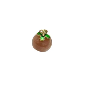 Persimmon-shaped sunstone crystal pendant with golden leaves on white background