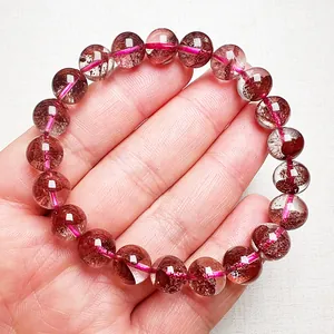 Makroaufnahme eines 10 mm roten Erdbeerquarz Kristallarmbands auf einer Handfläche