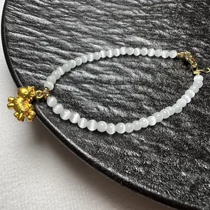 Detail van witte kattenoog kralenarmband met een gouden paardenhanger en sluiting