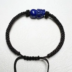 Detailed close-up of hand-carved blue lapis lazuli PiXiu on a black woven cord bracelet
