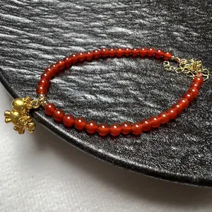 Detail van een rode agaat kralenarmband met een gouden dierenhanger en sluiting