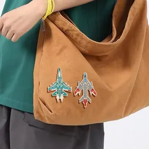 Détail de pin's en émail avion de chasse bleus et gris sur un sac en toile marron