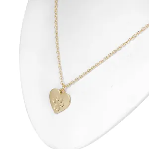 Detail of a gold heart pendant with paw print engraving on a white display stand