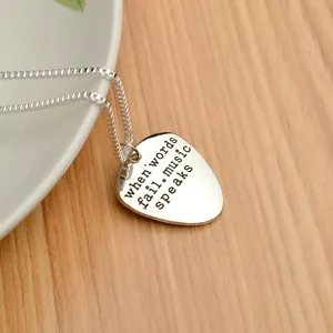 Silver guitar pick necklace with When Words Fail Music Speaks engraving on wood