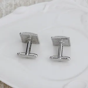 Macro view of square silver cufflinks with textured back on white ceramic plate
