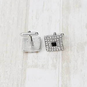 Gemelli quadrati in argento con pietre nere e cristalli su sfondo in legno